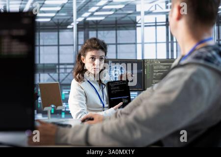 Programmers using tablet in data center, coordinating deployment of server architecture, improving data processing speed. Server farm IT professionals configuring and testing hardware using device Stock Photo
