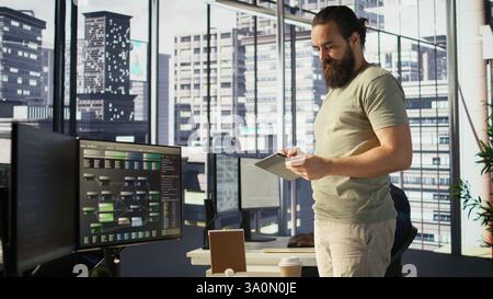 System administrator checking results on tablet after creating complex machine learning models that can process and analyze vast amounts of data. Admin standing in office, looking at device, camera B Stock Photo
