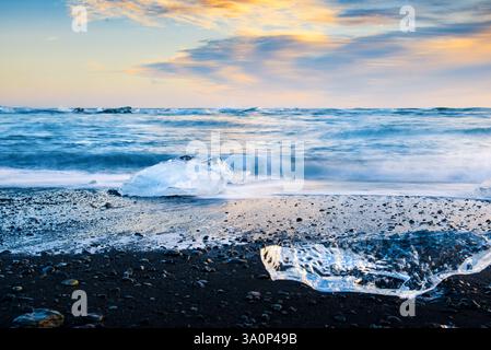 Diamond Beach in Iceland at sunset, where glistening ice chunks rest on black volcanic sand. A long exposure captures the smooth motion of waves, crea Stock Photo