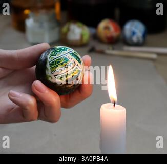 Female hand holding painted Easter egg near a candle. The process of painting eggs. Removing the wax. Egg is painted with various geometric patterns. Stock Photo
