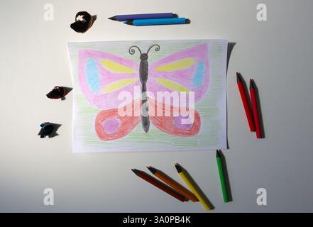 Photo of child's drawing with colored pencils. In the picture is butterfly. Colored pencils and shavings from pencil sharpening next to each other. Pi Stock Photo