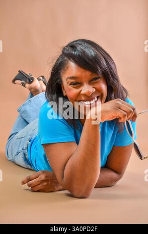 Studio portrait of a cheerful african american woman lying on the floor, holding sunglasses and smiling Stock Photo