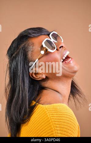 Studio portrait of a cheerful black woman wearing stylish sunglasses, laughing with her head tilted back Stock Photo