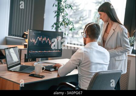 Two office workers are analyzing graphs that on the computer screen. Stock Photo