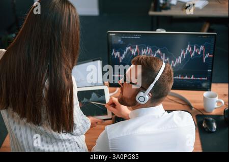 Two office workers are analyzing graphs that on the computer screen. Stock Photo
