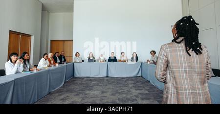A black female presenter speaking to a diverse team in a conference room setting, fostering collaboration and discussion. Stock Photo