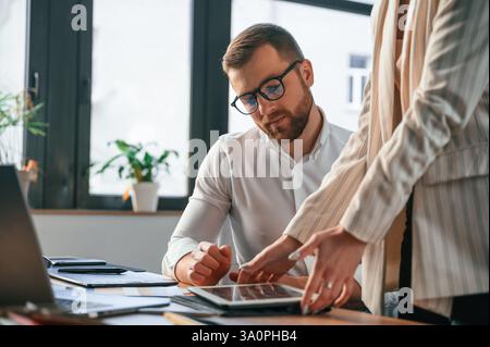 Woman is holding tablet, analysing information. Two employees are working together in the modern office. Stock Photo