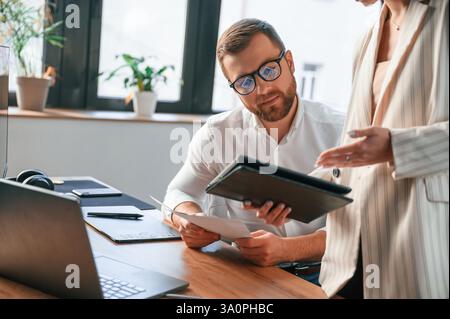 Woman is holding tablet, analysing information. Two employees are working together in the modern office. Stock Photo