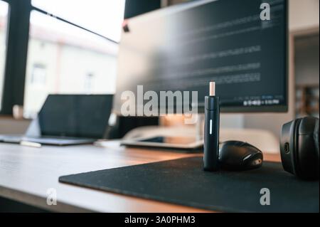 Close up view of electronic cigarette, mouse for computer, laptop and monitor with programming language code on it. Stock Photo