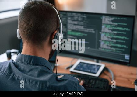 Software developer is writing code. Man in formal clothes is working in the modern office. Using computer. Stock Photo