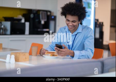 Hungry busy man having snack and scrolling online on smartphone Stock Photo