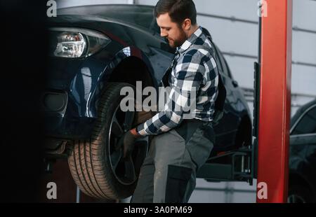Holding and changing new tire. Man in uniform is working in the auto salon. Stock Photo