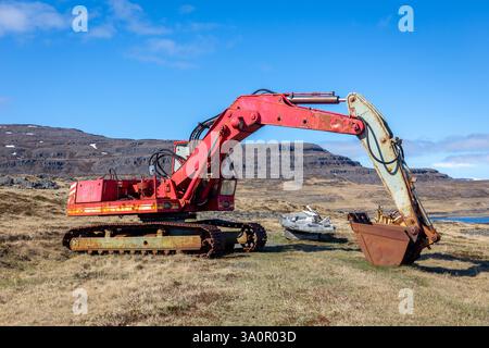 Old red rusty crawler excavator abandoned on the shore of Westfjords, Iceland with mountains in the background. Stock Photo