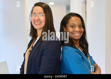 Portrait featuring a dentist and a manager standing back to back, both smiling confidently in a bright, modern dental clinic Stock Photo