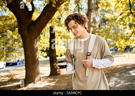 A handsome student with curly hair sips coffee, surrounded by bright autumn foliage and sunshine. Stock Photo