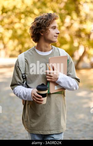 Handsome student carrying a coffee cup and notebooks while strolling in a vibrant autumn setting. Stock Photo