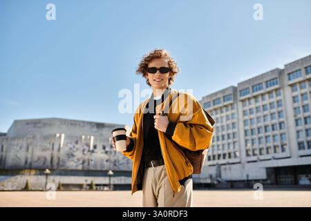 Confident young man with curly hair sips coffee, exuding charm under blue skies. Stock Photo