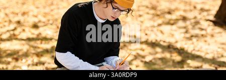 A fashionable young man sits on a bench in a park, focused on writing notes with a pencil. Stock Photo