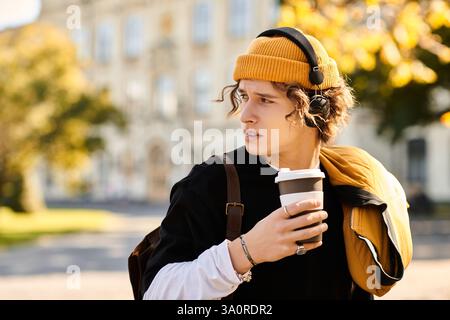 A stylish man with headphones sips coffee outside on a sunny day. Stock Photo