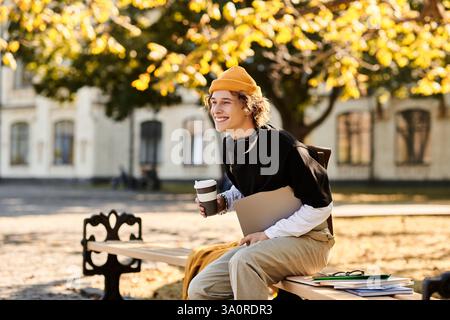 A young man in stylish clothes relaxes on a bench with coffee, studying outdoors. Stock Photo