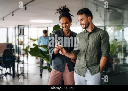 Diverse team of two business people working talking using smart phone walking in corporate office Stock Photo