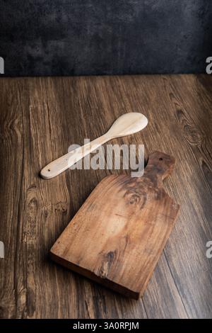 A rustic wooden cutting board and spoon placed on a textured wooden table, creating a warm and natural kitchen setting. Stock Photo