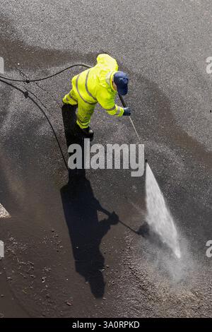 Road worker wearing high visibility clothing cleaning asphalt with high pressure water jet. High angle view Stock Photo