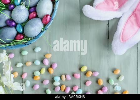 Naturally dyed blue Easter eggs in a basket with bunny ears and candy in background. Selective focus with blurred background. Stock Photo