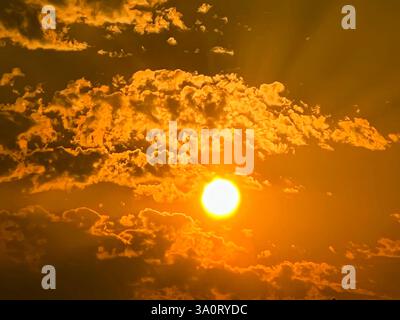 A stunning view of the sun shining through a dramatic sky filled with golden clouds. Captured during the golden hour, this image showcases warm tones Stock Photo