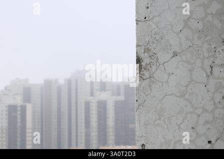 Fragment of an unrepaired wall and a blurred background on the left with silhouettes of houses in the distance for text or insertion Stock Photo
