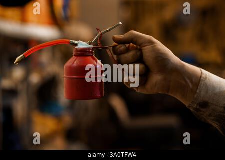 Red Oil Can Held by Worker with Dirty Hand in Workshop Environment. Stock Photo