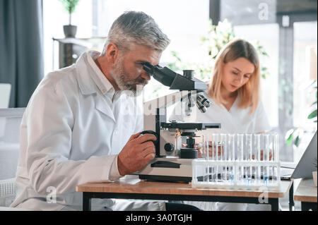 Focused on work. Two doctors are indoors together. Senior man with young woman. Stock Photo