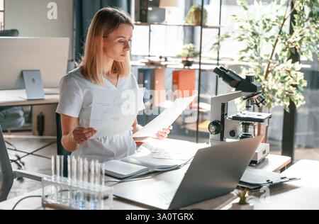 Young female doctor in coat is sitting in the clinic and working. Stock Photo