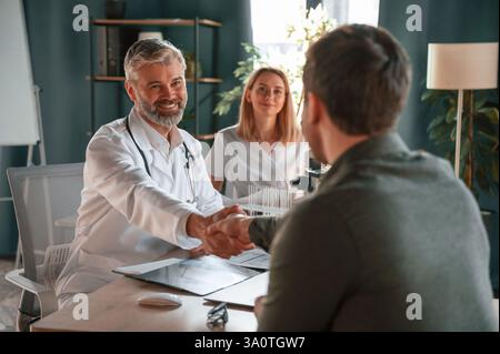 Greetings, making handshake. Two doctors consult a patient in a clinic. Stock Photo