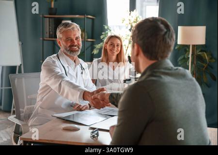 Greetings, making handshake. Two doctors consult a patient in a clinic. Stock Photo