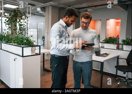 Information in the tablet. Two men are working in the modern office together. Stock Photo