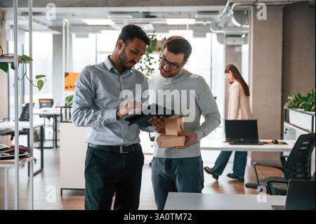 Holding eco boxes and tablet. Men and woman are working in the office together. Stock Photo