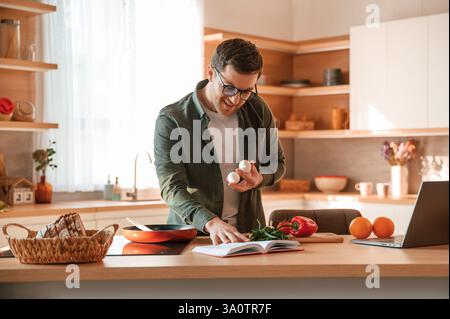 Holding two eggs in hand. Handsome man is on the kitchen at daytime. Stock Photo