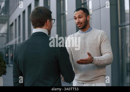Businessman in formal clothes is with black man outdoors in the city. Stock Photo