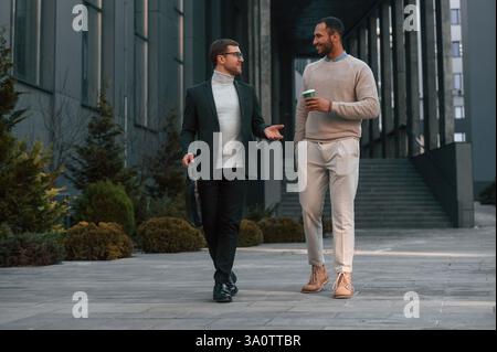 Walking and talking. Businessman in formal clothes is with black man outdoors in the city. Stock Photo