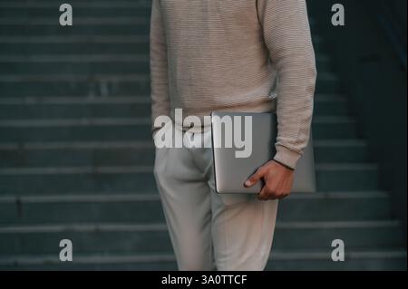 Close up view of man that is standing against the stairs outdoors and holding laptop. Stock Photo