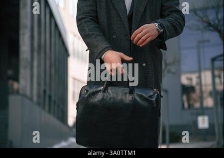 Man in black formal wear is standing outdoors and holding bag. Stock Photo