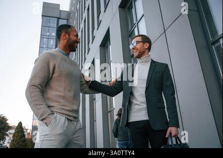 Conception of collaboration. Businessman in formal clothes is with black man outdoors in the city. Stock Photo