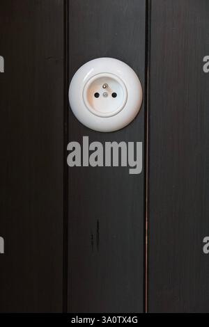 stylish historical design electrical outlet in white on black wooden paneling Stock Photo