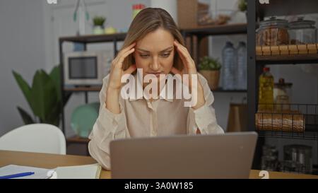 Woman concentrating in office indoors, looking stressed while working on laptop with hands on temples, surrounded by shelves and plants. Stock Photo