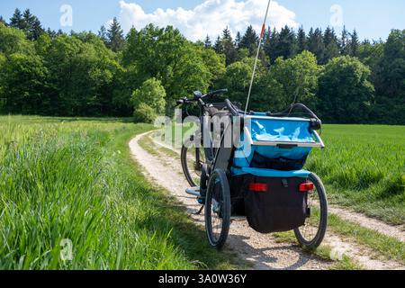 A bicycle with a child trailer parked on a winding dirt path through lush green fields, surrounded by nature and adventure. Stock Photo