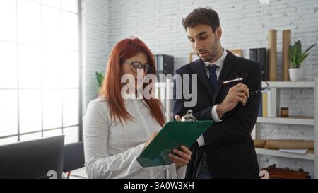 Hispanic business partners, man and woman, collaborating at the office indoors, analyzing documents, portraying teamwork in a professional workplace s Stock Photo