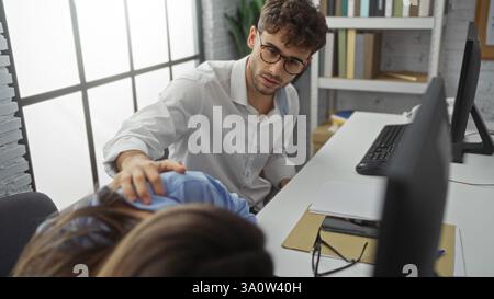 Man comforting woman in modern office setting, suggesting teamwork and support among colleagues indoors, showcasing employee dynamics in a corporate e Stock Photo