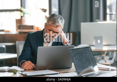 Feeling bad, tired, having headache, stressful. Senior businessman is working in the office. Stock Photo