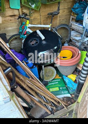 A garden shed full of things in disarray with a barbecue in prominent position Stock Photo